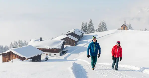 Mann und Frau spazieren durch die verschneite Winterlandschaft in den Bergen des Montafons