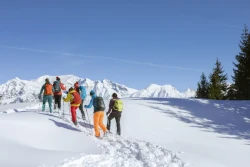 6 Menschen in Schneeanzügen wandern durch den Schnee bei schönem Wetter und blauem Himmel
