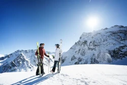 Mann und Frau in Schneekleidung stehen mit Skiern in der Hand auf einer Skipiste in den Bergen und unterhalten sich