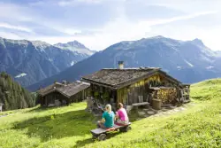 Zwei Wanderer sitzen im Montafon auf einer Bank neben einer Hütte und genießen die Aussicht