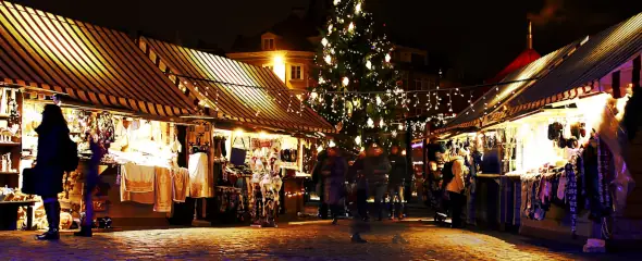 Stände auf einem beleuchteten Weihnachtsmarkt und ein großee Weihnachtsbaum